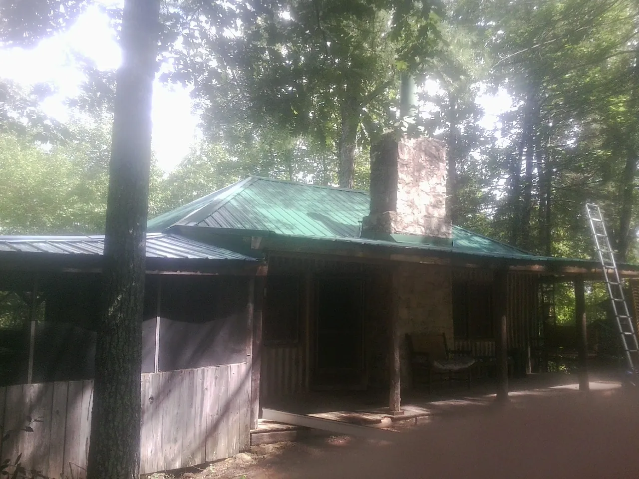Green metal roof and stone chimney above a log cabin porch in Barton