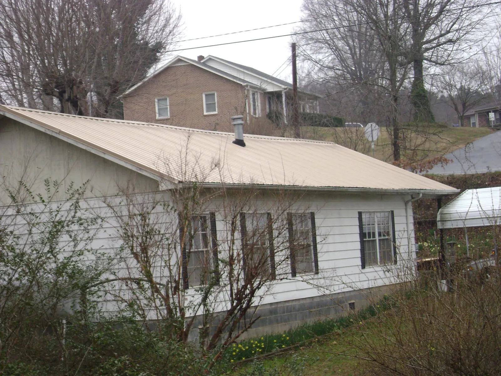 Tan metal roof on a white sided house set into a hillside — Commercial Roofing by Roofing Brothers in Barton