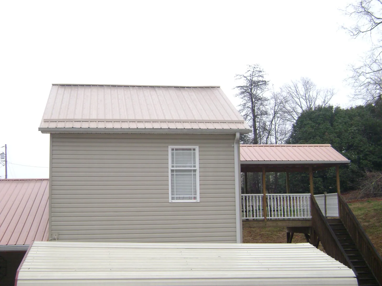 Tan metal roofs on a two story addition and attached porch, from a Roof Replacement job in Barton